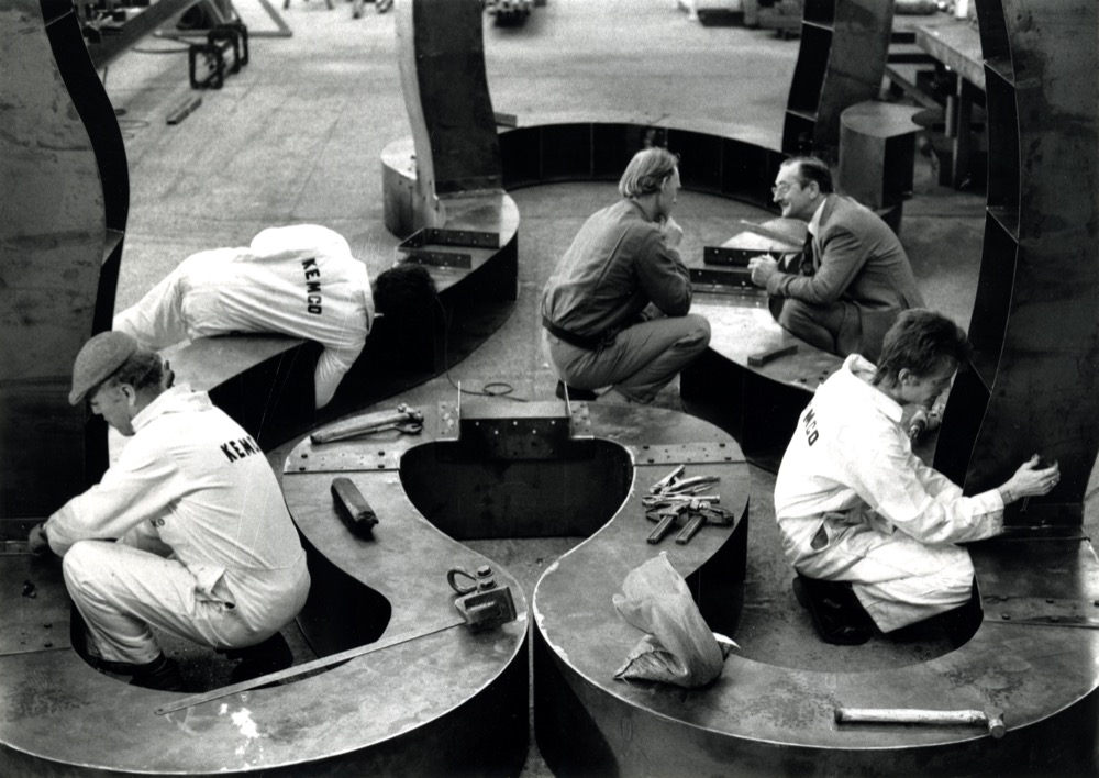‘Richard Deacon in discussion with Griff Jones at Kemco fabrications in 1985. Gary Chapman has his back to the camera leaning across the sculpture on left hand side. Still taken during the filming of 'Wall of Light, dir. John Tchalenko